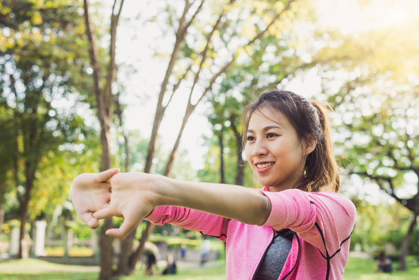 Detailní záběr mladé ženy zahřívá své tělo tím, že si protáhne paže, aby byla připravena na cvičení a jógu v parku obklopen přírodou a teplou lehkou odpolední oblohou. Koncept outdoorového cvičení - Fotografie, Obrázek