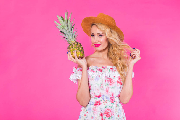 Happy young woman holding a pineapple on a pink background. Summer, diet and holidays concept - Photo, Image