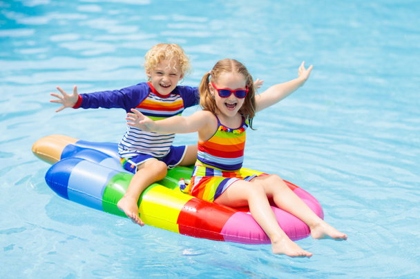 Boy and girl on inflatable ice cream float in outdoor swimming pool of tropical resort. Summer vacation with kids. Swim aids and wear for children. Water toys. Little child floating on colorful raft. - Foto, afbeelding