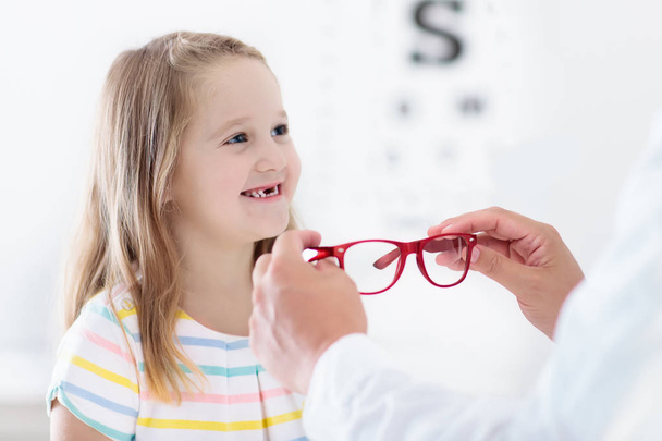 視力検査の子。光学店で眼鏡を選ぶ小さな子供。小学生の視力測定。子供用のアイウェア。ドクター・パフォーマンス・アイチェック。女の子とともに眼鏡で手紙チャート. - 写真・画像