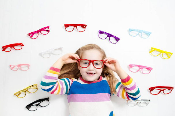 Criança à vista dos olhos. Um miúdo a escolher óculos na loja de óptica. Medição de visão para crianças da escola. Vestido de olho para crianças. Médico a verificar os olhos. Menina com óculos na carta
. - Foto, Imagem