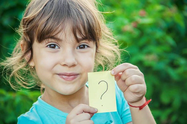 Ребенок держит лист бумаги с вопросительным знаком. Селективный фокус
. - Фото, изображение
