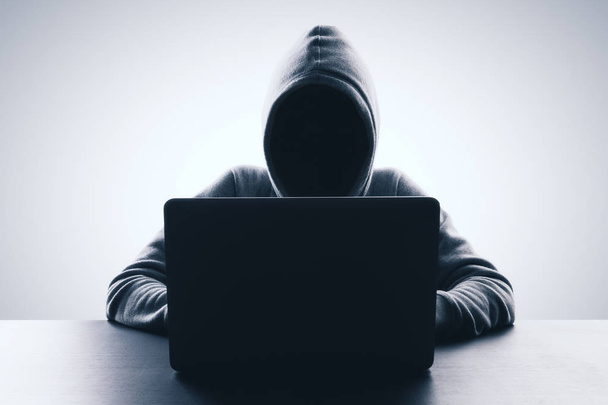 Man with hood using laptop on gray background. Hacker and web attack concept. Copy space  - Fotografie, Obrázek