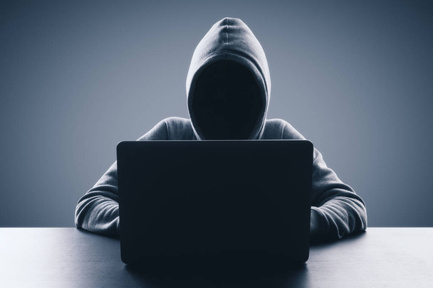 Man with hood using laptop on gray background. Hacker and virus concept. Copy space  - Photo, image