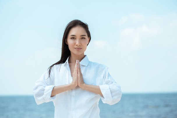 focused asian woman doing namaste mudra gesture in front of sea  - Photo, Image