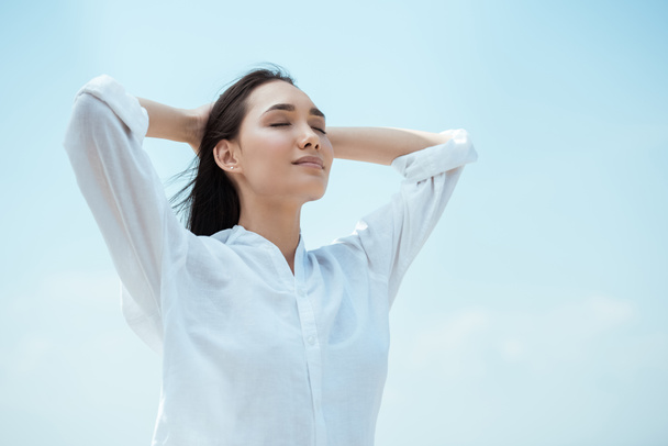 low angle view of young asian woman with closed eyes against blue sky  - Foto, immagini