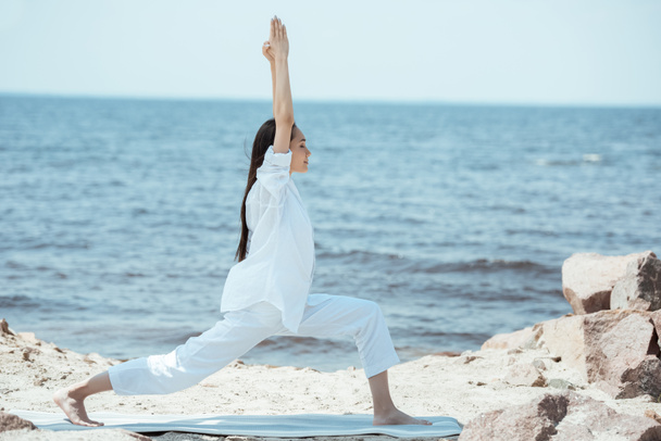 Asyalı kadın virabhadrasana (Ben poz savaşçı) görünümünü yoga mat deniz yan - Fotoğraf, Görsel