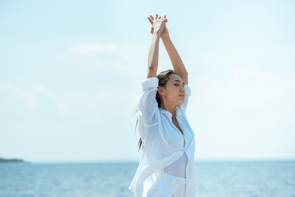 attractive asian woman with closed eyes standing with wide arms in front of sea  - Photo, Image