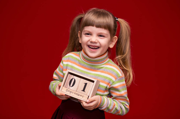 Muotokuva iloinen pieni tyttö eristetty punainen pidä puinen kalenteri asetettu ensimmäinen syyskuu. Takaisin kouluun.
 - Valokuva, kuva