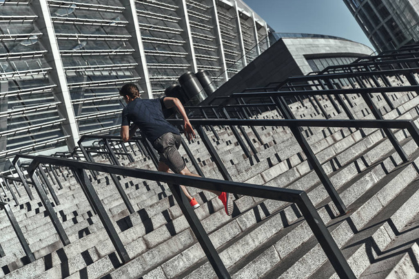 full length, back view of man in sports clothing running on stairs at stadium  - Zdjęcie, obraz