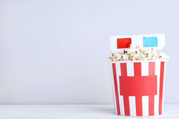 Popcorn in striped bucket with glasses on grey background - Φωτογραφία, εικόνα