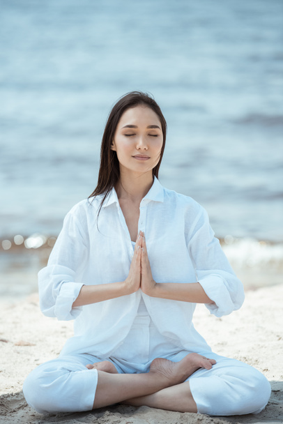 young asian woman in anjali mudra (salutation seal) pose on beach  - Photo, Image