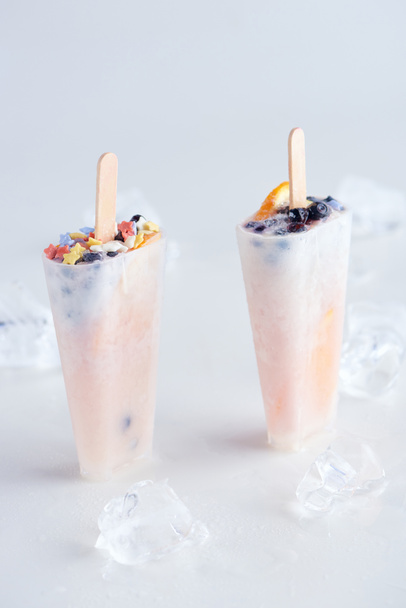 vista ravvicinata di ghiaccioli dolci fatti in casa con frutta e bacche e cubetti di ghiaccio su grigio
   - Foto, immagini