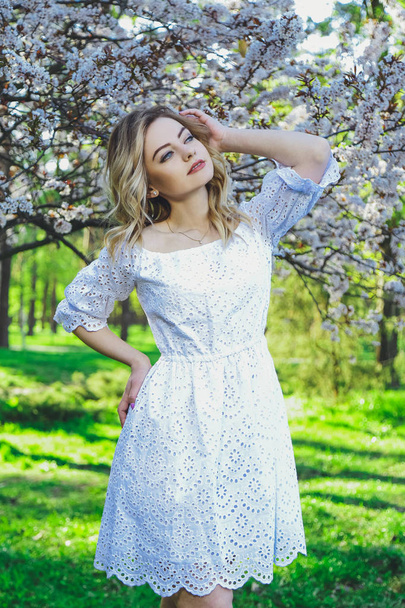 Beautiful blonde girl with blond hair in a dress on a background of spring blooming trees - Φωτογραφία, εικόνα