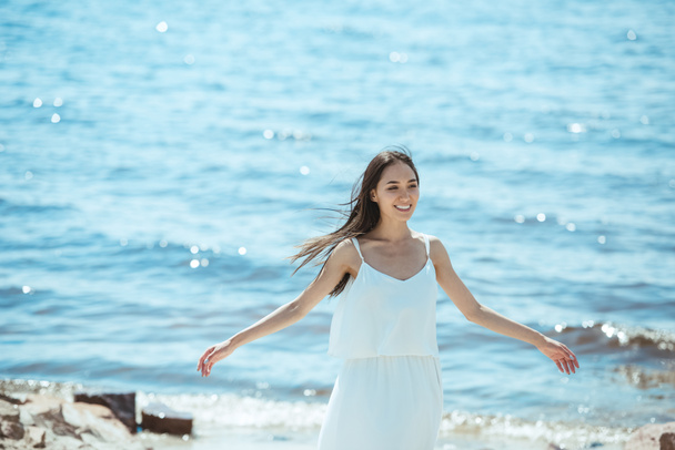 glückliche asiatische Frau im weißen Kleid mit breiten Armen am Meer stehend  - Foto, Bild