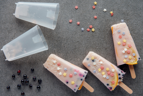 top view of sweet cold fruity popsicles, colorful stars and berries on grey - Фото, изображение