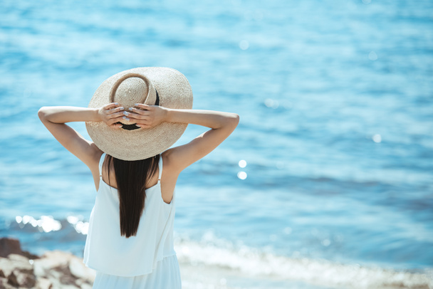 vue arrière de la femme en robe blanche et chapeau de paille debout devant la mer
  - Photo, image