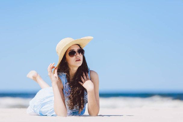 Pretty girl laying on beach, wearing hat and sunglasses. Sunbathing. Sunny summer. - Foto, immagini