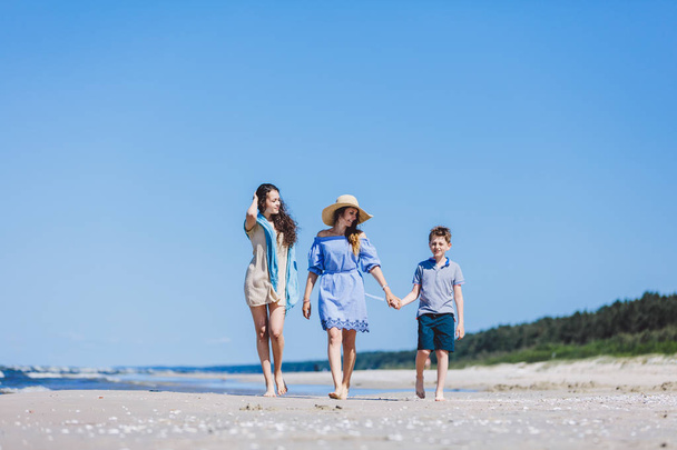 Η μητέρα με τα παιδιά με τα πόδια από τη θάλασσα στην καυτή θερινή ημέρα. Συγκόλληση οικογένεια. - Φωτογραφία, εικόνα