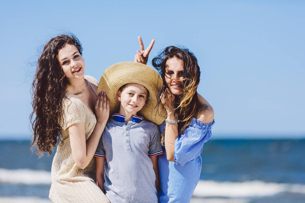 Mãe, filha e um rapaz de chapéu de palha a brincar na praia. Ligação familiar
. - Foto, Imagem