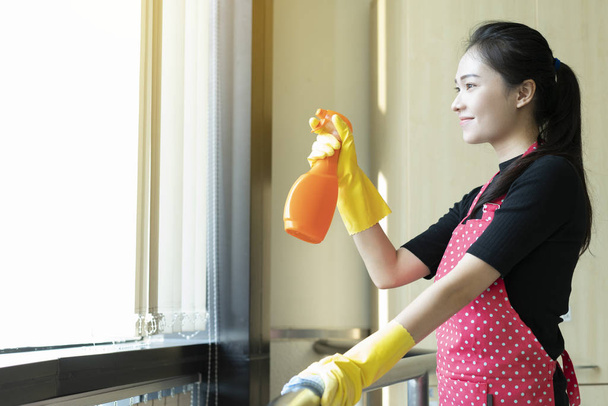 счастливая азиатка в перчатках уборка с моющим спреем в окно дома
 - Фото, изображение