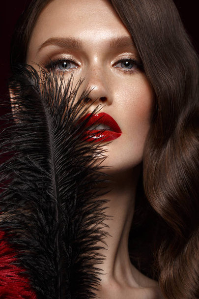 A beautiful girl with evening make-up, a Hollywood wave and a black feather in her hand. Beauty face. - Foto, immagini