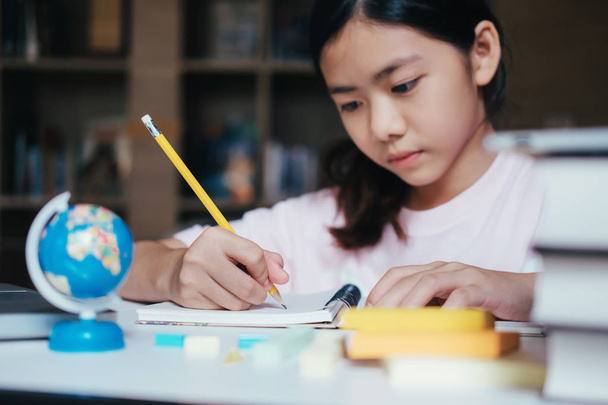 Концепция образования. Девочка читает, пишет и делает домашнее задание в библиотеке школы. Учиться и учиться
 - Фото, изображение