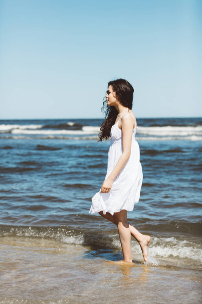 Girl in white dress walking by seashore - Zdjęcie, obraz