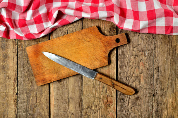 Cuchillo sobre tabla de cortar de madera y un marco superior de mantel a cuadros rojo sobre fondo de mesa de madera
 - Foto, imagen