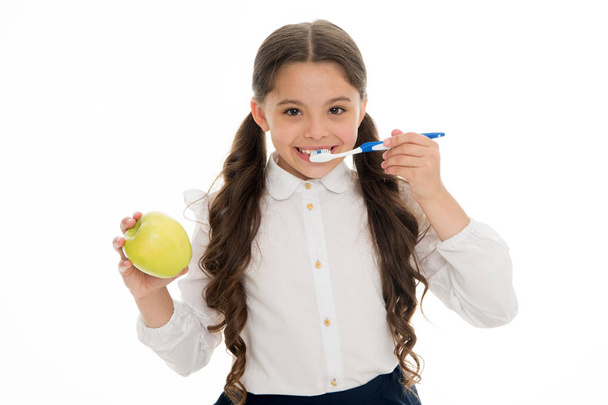 Oral hygiene. Girl cute holds toothbrush and apple white background. Child girl holds apple and brush tooth with paste. Child school girl smart kid happy face cares hygiene. Brush teeth concept - Foto, Imagem