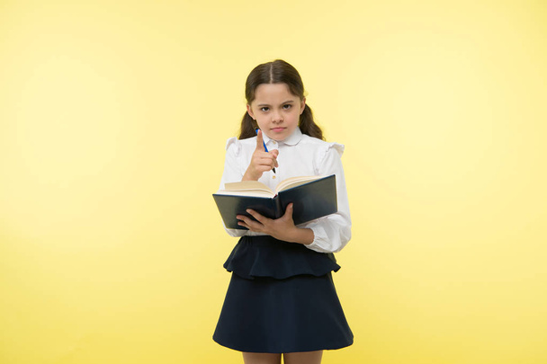 You better know it. Child school uniform smart kid done with homework. Girl cute serious face yellow background. Child girl school uniform clothes holds book and pen. Check knowledge concept. - Photo, Image