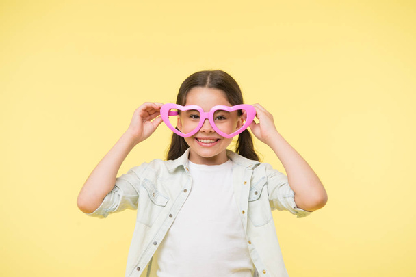 Happy child wear heart shaped glasses on yellow background. Little girl smile in fashion accessory. Summer fashion look. Funky style beauty. Young and confident. Valentines day. I love you - Foto, afbeelding