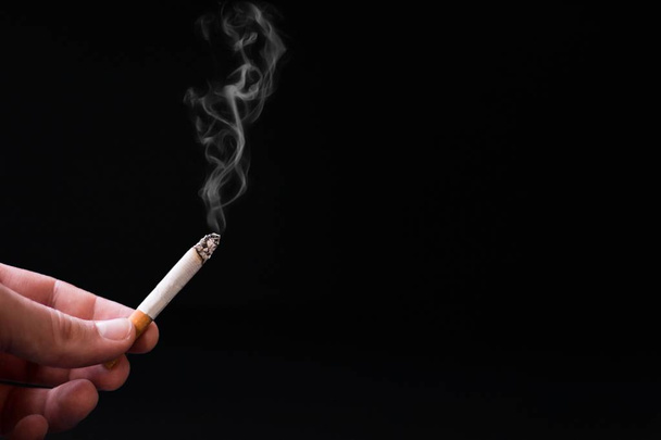 人間の手は、暗い黒いバック グラウンドにたばこを保持しています。停止喫煙と健康ケアの概念。世界はタバコの日.                                - 写真・画像