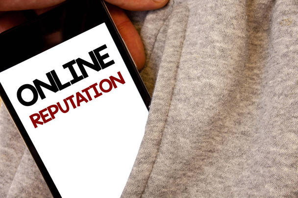 Text sign showing Online Reputation. Conceptual photo Reliability Ranking Review Evaluation Satisfaction Quality Words written black Phone white Screen Hand holding pocket white tracksuit - Photo, Image