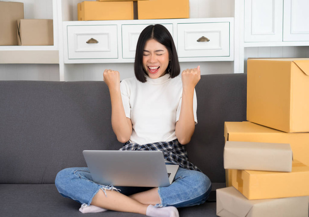 Szczęśliwy młody Asian kobieta dorywczo celebracja sukces w pracy dla firm poszukujących online z laptopa. MŚP, pojęcie dostawy. Rozpocząć się właścicielem małej firmy - Zdjęcie, obraz