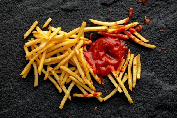Papas fritas con salsa de tomate sobre fondo de piedra oscura
 - Foto, imagen
