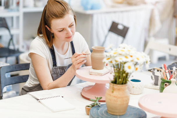 Майстерня кераміки з глини, жінка прикрашає посуд горщик
 - Фото, зображення