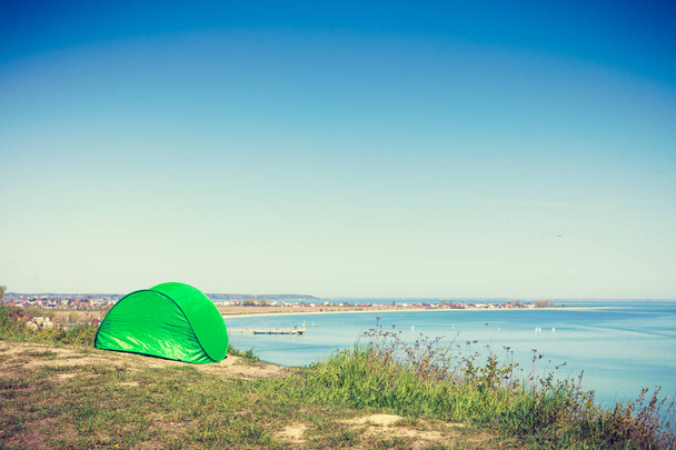Tourism and recreation. Small green tent in natural area surrounded by meadow water sea lake. - Foto, imagen