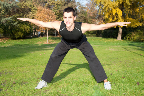 Attractive young man doing exercise in autumn park - Foto, Imagem