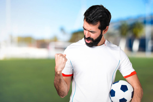 Щасливий футболіст тримає футбольний м'яч на футбольному полі
 - Фото, зображення