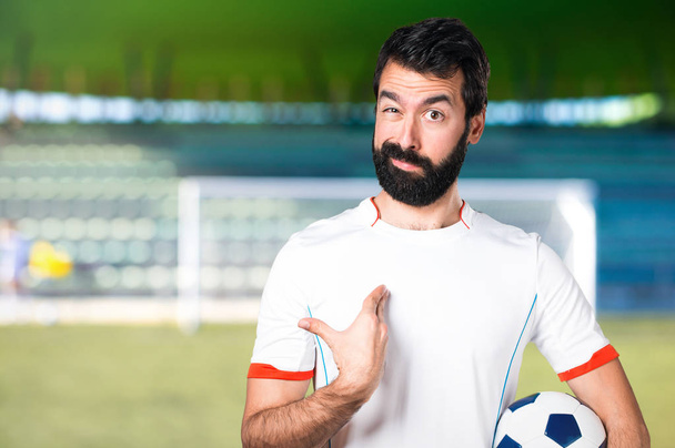 Jogador de futebol segurando uma bola de futebol fazendo gesto surpresa em um campo de futebol
 - Foto, Imagem