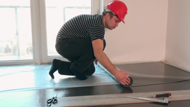 constructor man met rode helm leggen ondervloer voor laminaat vloeren installatie - Video