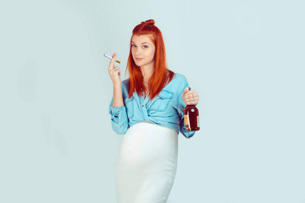 Young careless girl with ginger hair waiting for baby and standing with cigarette and alcohol on light blue background. Mixed race model, latin hispanic irish woman - Foto, immagini
