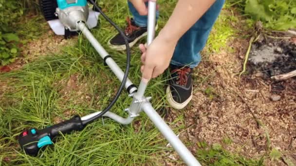 Egy ember összegyűjti a fogantyú string trimmer, a kertjében. - Felvétel, videó