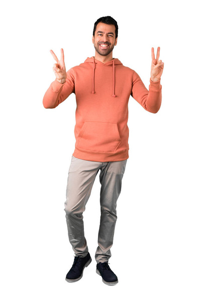 Full body of Man in a pink sweatshirt smiling and showing victory sign with both hands and with a cheerful face on isolated white background - Foto, immagini