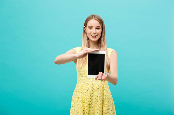 Pretty smiling woman showing blank black screen of digital tablet. Isolated over blue background. - Foto, Imagen