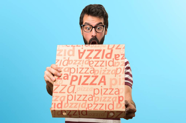 Zaskoczony mężczyzny w okularach, trzymając pizze na kolorowe tło - Zdjęcie, obraz