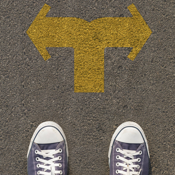 Par de zapatos de pie en una carretera con flecha amarilla de dos vías
 - Foto, imagen