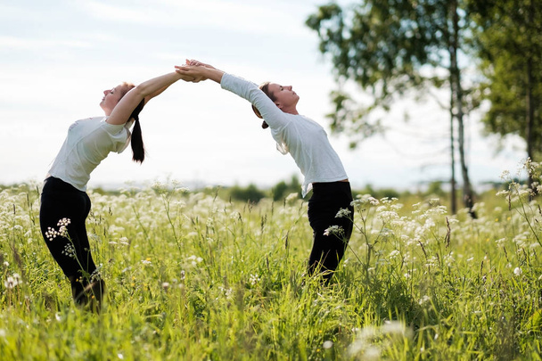 Két nő le csinál jóga gyakorlatok, állandó hajlító egymást a szabadban, természetvédelmi. - Fotó, kép