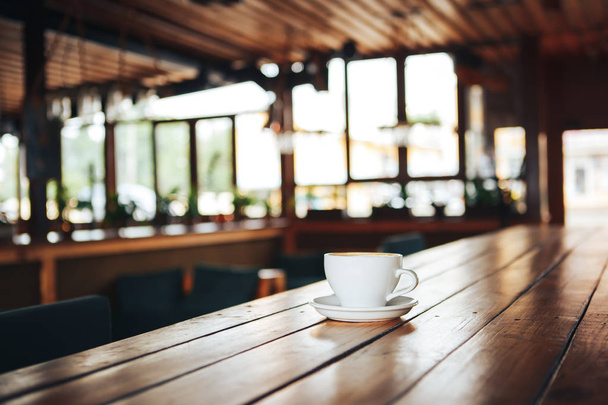 Warme koffie in witte cup op houten tafel. Witte kopje koffie op een houten tafel in een café. Goedemorgen met een keramische witte kop koffie in een café  - Foto, afbeelding